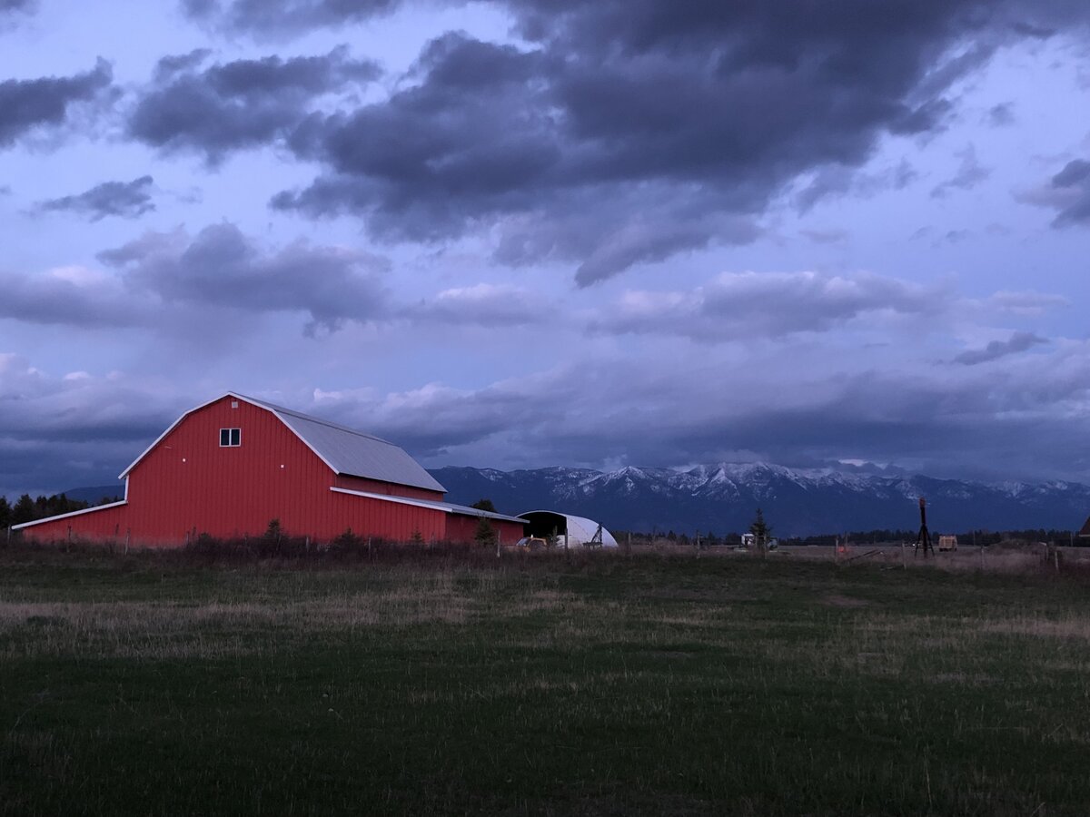 Dark clouds above a red barn near Kalispell, Montana, the Rocky Mountains in the background.